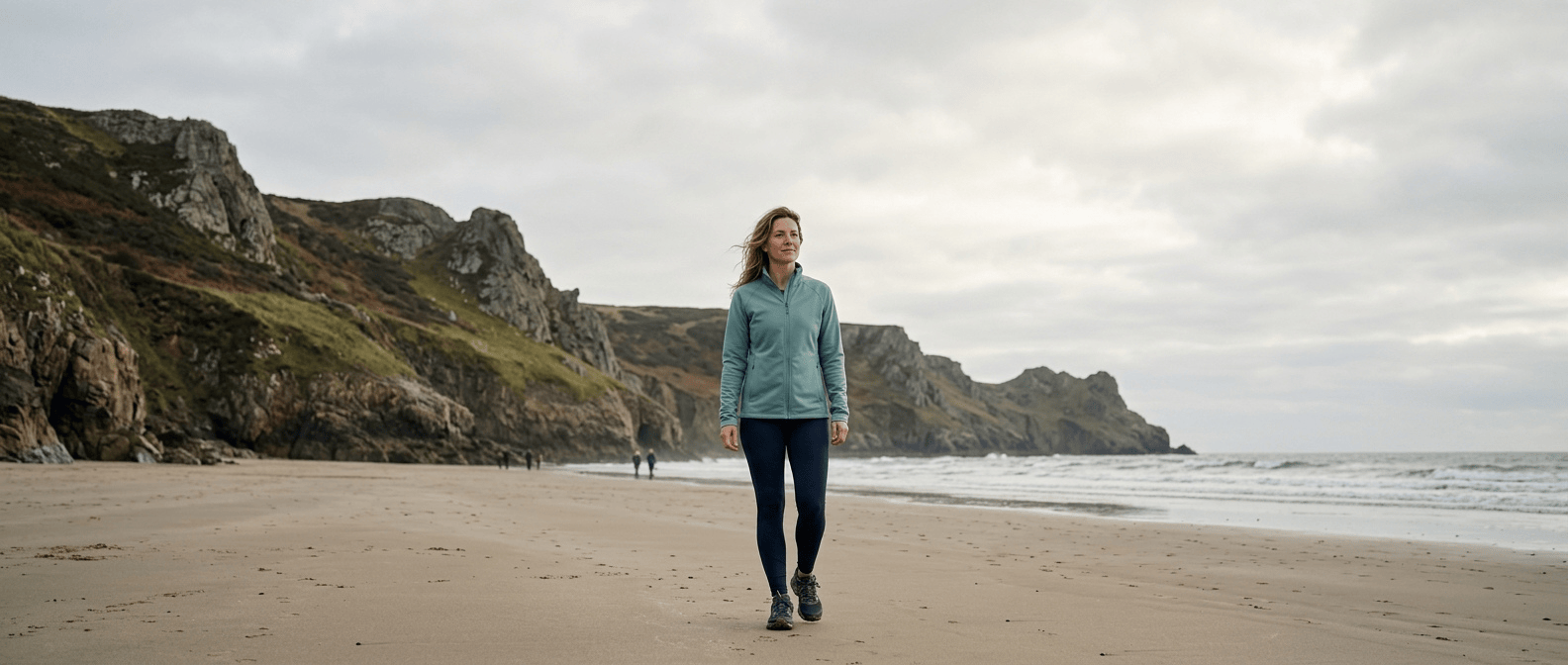 A woman walking confidently on a sandy Gower Peninsula beach, representing the results of private weight loss treatment at Medihub Pharmacy Swansea